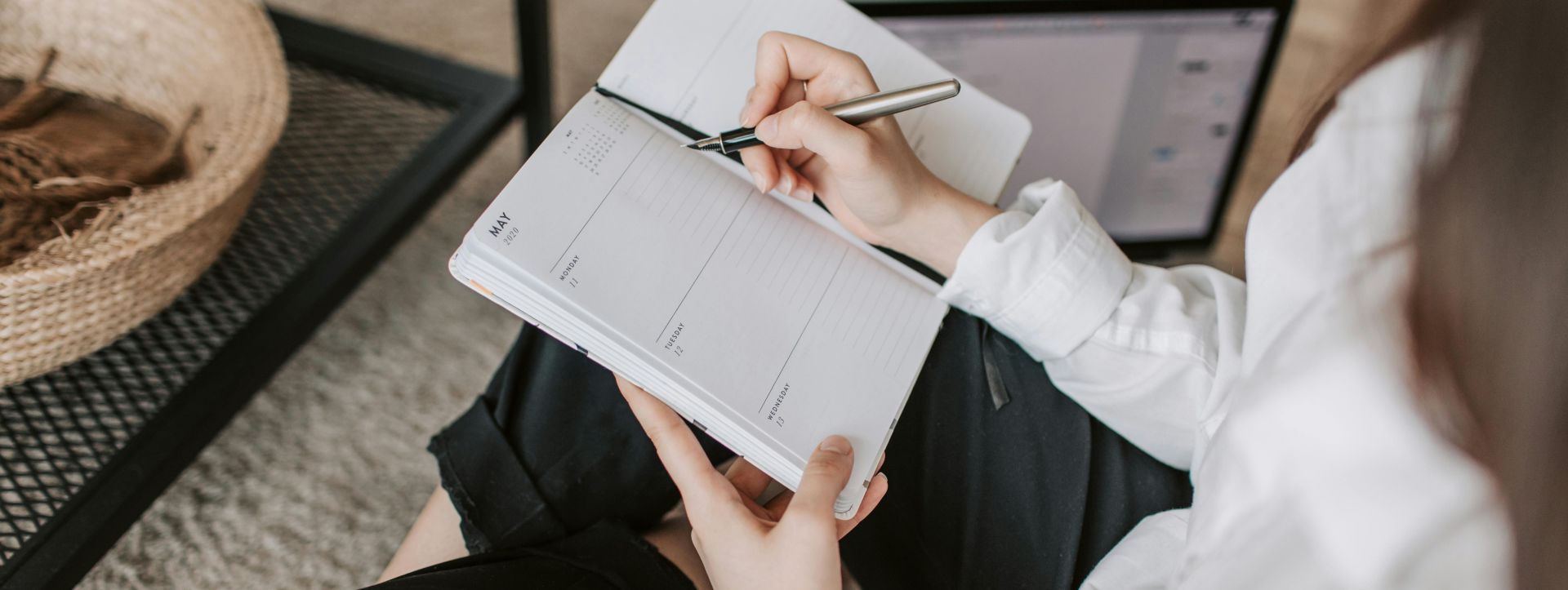 Side view of faceless woman in casual clothes taking notes on notepad while sitting in lotus pose on floor in modern apartment during daytime